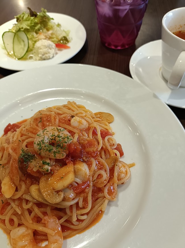 トマトパスタ。サラダとスープのセット。パスタの上には海鮮が乗っている