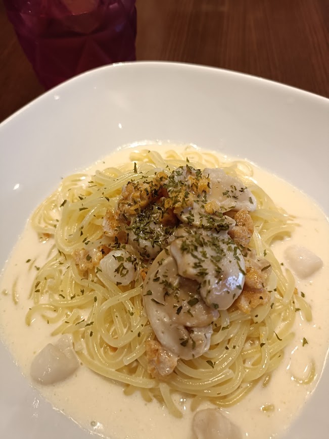 ウニのクリームパスタ。白い器に白いクリームソース。貝柱と魔手ルームにウニが乗っている