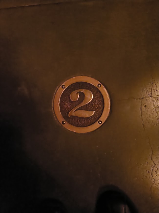 コンクリートの床に埋め込まれた、真鍮製で丸い枠の数字「2」のプレート