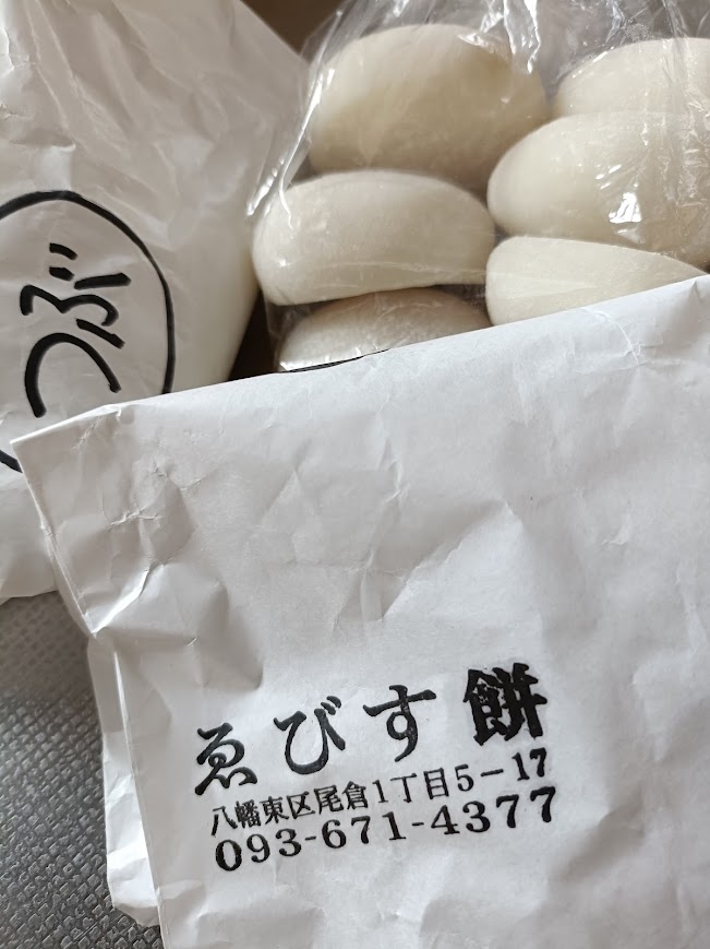 白いお餅が袋に入っている。奥に「つぶ」と書かれた紙袋と、手前に「えびす餅」住所と電話番号のスタンプが押された袋
